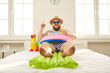 © Studio Romantic - Happy young man spends summer holidays in Covid pandemic quarantine. Chubby male tourist lying on bed with inflatable lifebuoy and beach mattress, drinking juice and enjoying 'stay at home' vacation