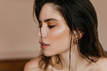 Close-up shot of inspired european woman with golden earrings. Indoor photo of interested brunette lady posing on brown background.