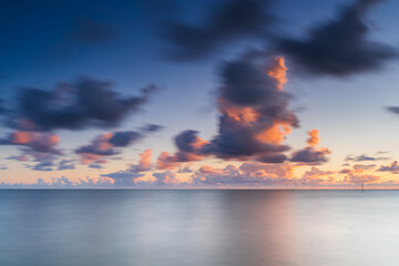 Wall Mural - Moving clouds above large lake with smooth water and a sunset view from the coast