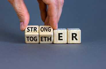 Stronger together symbol. Businessman turns cubes and changes the word together to stronger. Beautiful grey background, copy space. Business, motivational and stronger together concept.