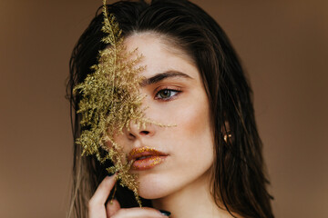 Sticker - Close-up shot of appealing girl holding green leaf near face. Portrait of attractive young lady standing on dark background.