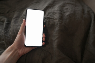 man hand holding phone with white screen over bed on background