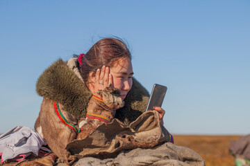 A young girl, in the national winter clothes of the northern inhabitants of the tundra, takes a selfie on a smartphone