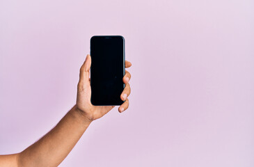 Hand of young hispanic man showing smartphone over isolated pink background.