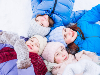 Wall Mural - A group of joyful children in bright packaging and knitted hats in winter lie in the snow and look up