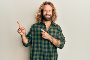 Handsome man with beard and long hair wearing casual clothes smiling and looking at the camera pointing with two hands and fingers to the side.