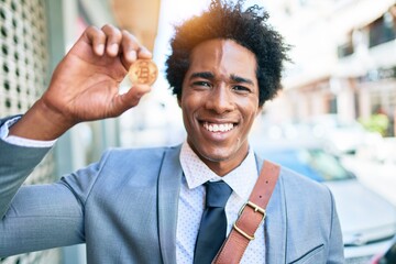 Wall Mural - Young handsome african american businessman wearing suit smiling happy. Standing with smile on face holding bitcoin at town street.