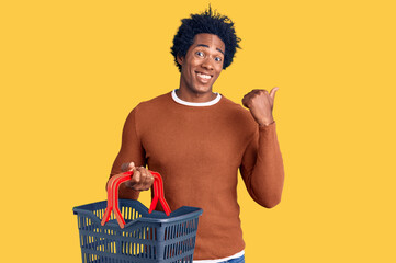 Wall Mural - handsome african american man with afro hair holding supermarket shopping basket pointing thumb up t