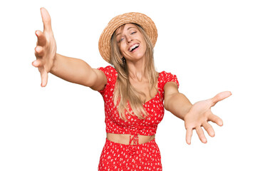 Poster - Beautiful caucasian woman wearing summer hat looking at the camera smiling with open arms for hug. cheerful expression embracing happiness.