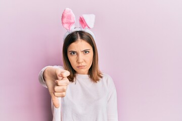 Sticker - Young beautiful woman wearing cute easter bunny ears looking unhappy and angry showing rejection and negative with thumbs down gesture. bad expression.