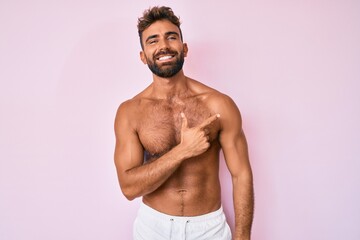 Wall Mural - Young hispanic man standing shirtless cheerful with a smile of face pointing with hand and finger up to the side with happy and natural expression on face