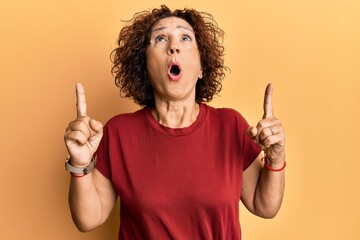 Poster - Beautiful middle age mature woman wearing casual clothes amazed and surprised looking up and pointing with fingers and raised arms.