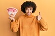 © Krakenimages.com - Young hispanic girl holding 20 israel shekels banknotes smiling happy and positive, thumb up doing excellent and approval sign