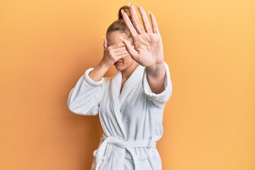 Sticker - Young blonde woman wearing bathrobe covering eyes with hands and doing stop gesture with sad and fear expression. embarrassed and negative concept.