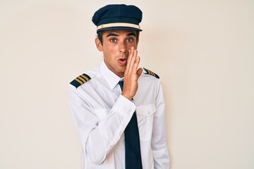 Sticker - Young hispanic man wearing airplane pilot uniform hand on mouth telling secret rumor, whispering malicious talk conversation