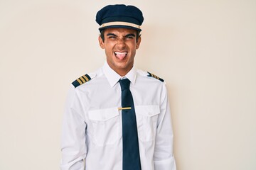 Sticker - Young hispanic man wearing airplane pilot uniform sticking tongue out happy with funny expression. emotion concept.