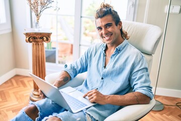 Wall Mural - Young hispanic man smiling happy using laptop at home