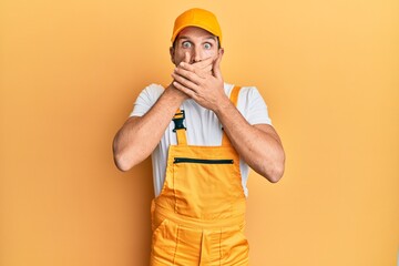 Poster - Young handsome man wearing handyman uniform over yellow background shocked covering mouth with hands for mistake. secret concept.