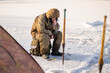 © sushytska - A fisherman sits on a box and catches fish in winter in sunny weather