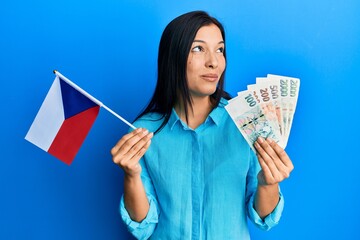 Sticker - Young latin woman holding czech republic flag and koruna banknotes smiling looking to the side and staring away thinking.