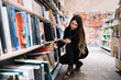 © GalakticDreamer - Young woman choosing books and listening to music in bookstore