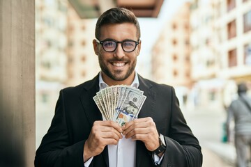 Wall Mural - Young hispanic businessman smiling happy holding american dollars at the city.