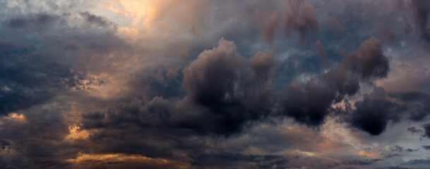 Wall Mural - wide panoramic view of the dramatic sunset sky with dark cumulus clouds and natural purple-orange illumination from the evening dawn. Artistic backdrop for atmospheric design or decoration
