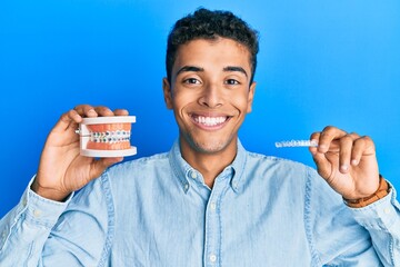 Wall Mural - Young handsome african american man holding invisible aligner orthodontic and braces smiling with a happy and cool smile on face. showing teeth.