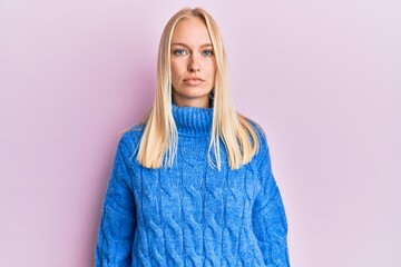 Wall Mural - Young blonde girl wearing wool winter sweater relaxed with serious expression on face. simple and natural looking at the camera.