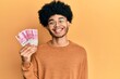 © Krakenimages.com - Young african american man with afro hair holding 100000 indonesian rupiah looking positive and happy standing and smiling with a confident smile showing teeth