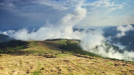 Wall Mural - Panoramic view of a mountain range in the fog in cloudy summer weather at sunset.