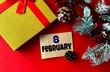 February 8 on craft paper. Near fir branches, cones, ribbon,gift box on a red background.Calendar for February.