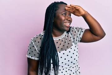 Canvas Print - Young black woman with braids wearing casual clothes very happy and smiling looking far away with hand over head. searching concept.