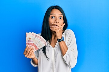 Wall Mural - Young african american woman holding 10 colombian pesos banknotes shocked covering mouth with hands for mistake. secret concept.