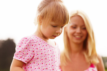 Young blonde mother in dress playing with little kid blonde daughter in the park.