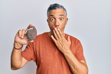 Sticker - Handsome middle age mature man holding pumice stone covering mouth with hand, shocked and afraid for mistake. surprised expression