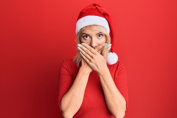 Poster - Young blonde girl wearing christmas hat shocked covering mouth with hands for mistake. secret concept.