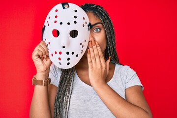 Canvas Print - Young african american woman with braids wearing hockey mask covering mouth with hand, shocked and afraid for mistake. surprised expression