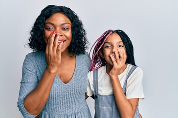 Poster - Beautiful african american mother and daughter wearing casual clothes and hugging laughing and embarrassed giggle covering mouth with hands, gossip and scandal concept