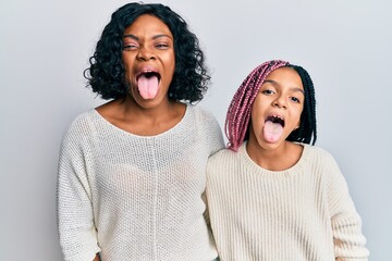 Poster - Beautiful african american mother and daughter wearing casual clothes and hugging sticking tongue out happy with funny expression. emotion concept.