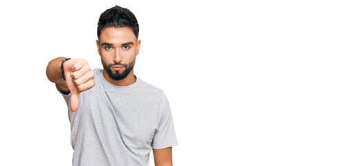 Canvas Print - Young man with beard wearing casual grey tshirt looking unhappy and angry showing rejection and negative with thumbs down gesture. bad expression.