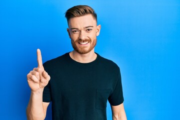 Young redhead man wearing casual black t shirt smiling with an idea or question pointing finger up with happy face, number one