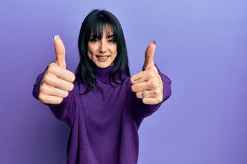 Young brunette woman with bangs wearing turtleneck sweater approving doing positive gesture with hand, thumbs up smiling and happy for success. winner gesture.