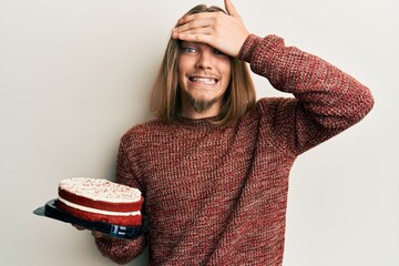 Wall Mural - Handsome caucasian man with long hair holding carrot cake stressed and frustrated with hand on head, surprised and angry face