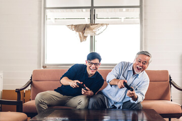 Wall Mural - Portrait of happy love asian family senior mature father and young adult son having fun enjoying holding gamepad controller play console video game together at home