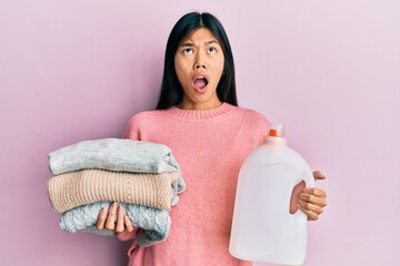 Sticker - Young chinese woman holding detergent bottle and clothes angry and mad screaming frustrated and furious, shouting with anger looking up.