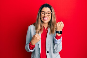 Beautiful brunette woman wearing business shirt and glasses celebrating surprised and amazed for success with arms raised and eyes closed