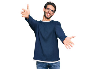 Wall Mural - Young hispanic man wearing casual clothes and glasses looking at the camera smiling with open arms for hug. cheerful expression embracing happiness.