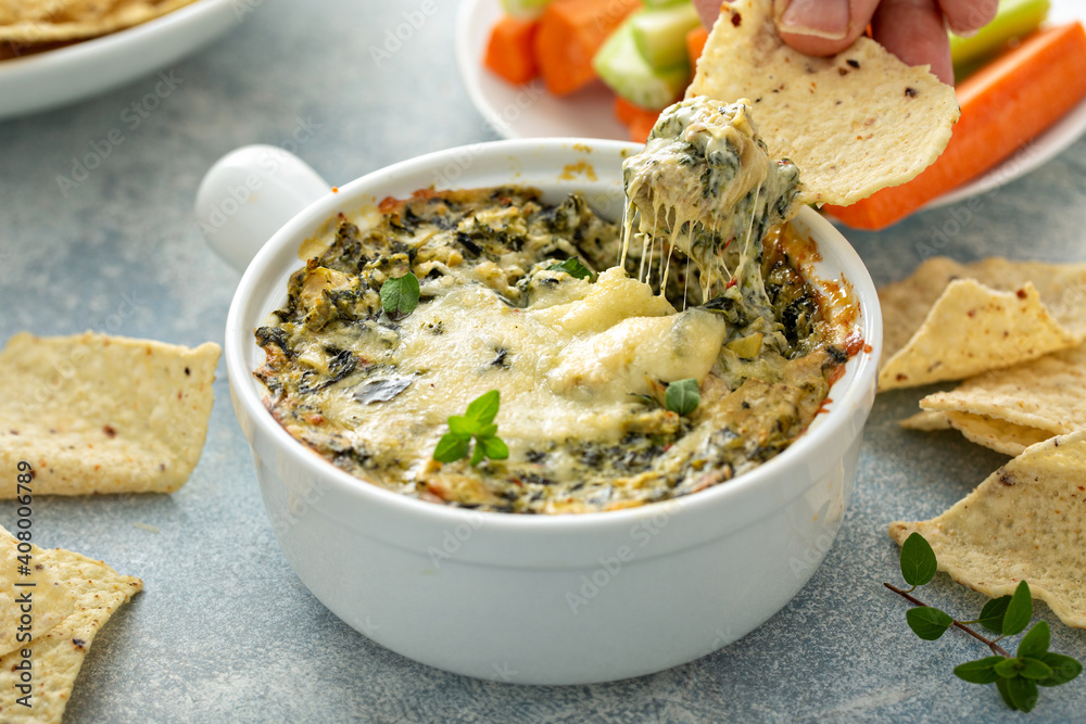 Artichoke spinach dip in a baking dish with a cheese pull - obrazy, fototapety, plakaty 
