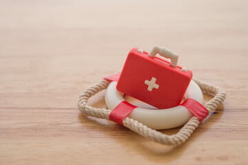 Red first aid kit doctor bag on lifebuoy with wooden background copy space. Health or life insurance, retirement planning, healthcare and medical concept. Worry free with the medical expense.